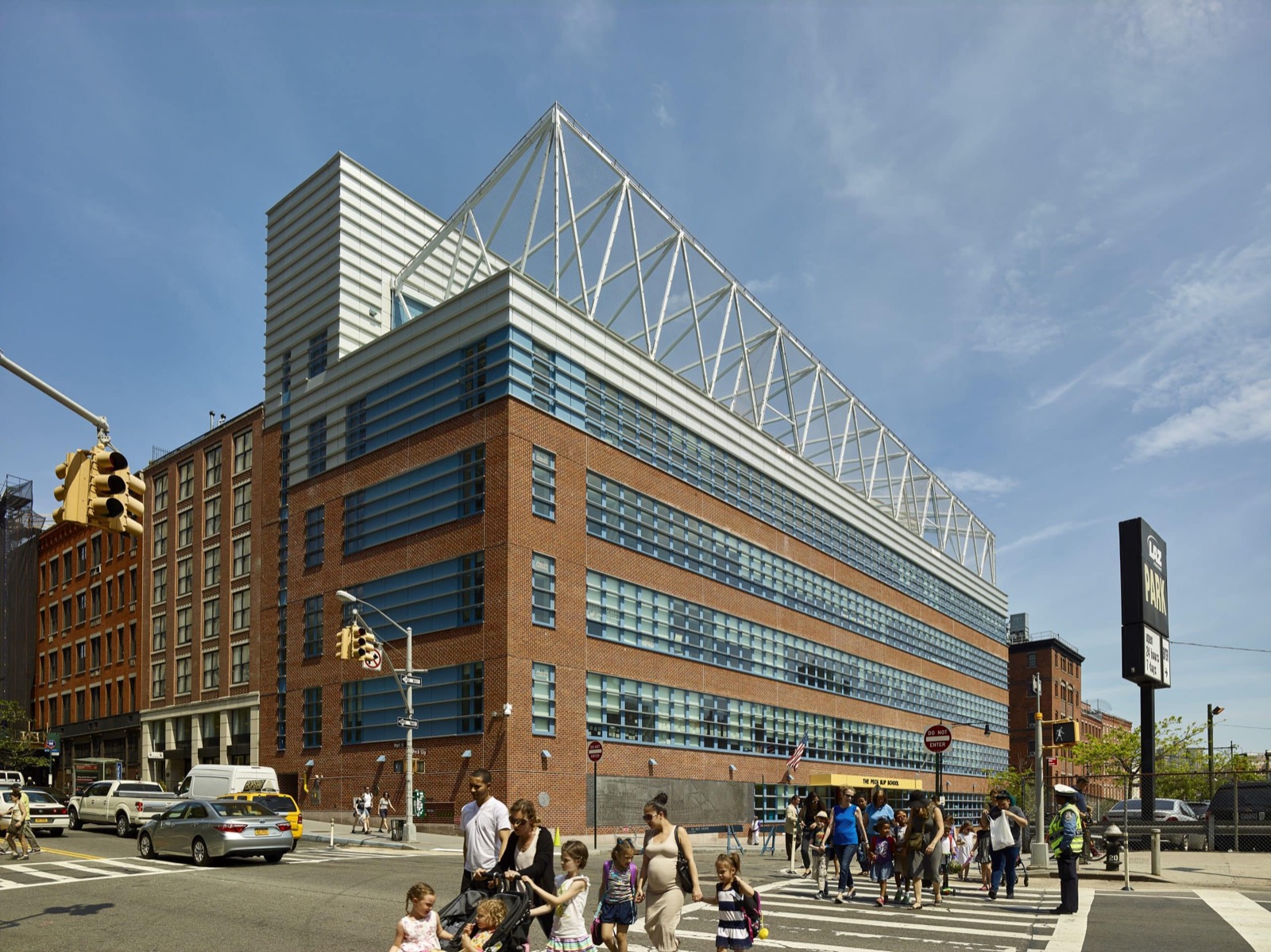 The Peck Slip School (PS 343), a modern brick building with a curved roof truss, families crossing the street in front